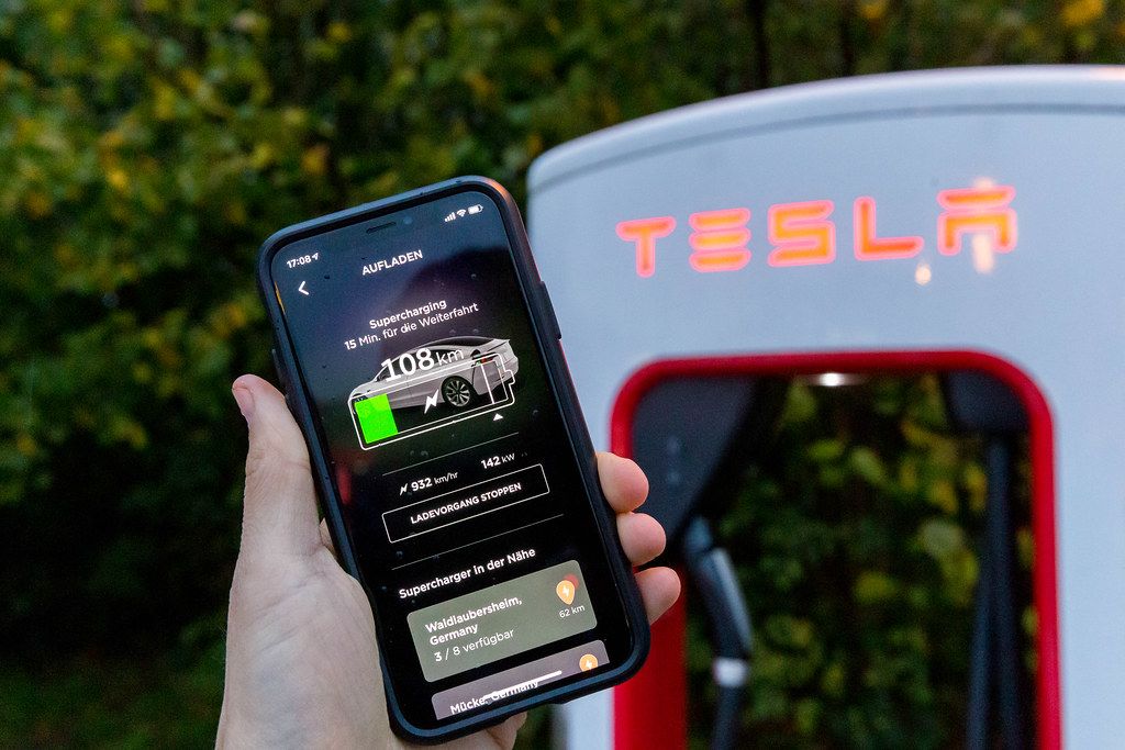 tesla-supercharging-in-the-smartphone-app-held-in-front-a-tesla-charging-station